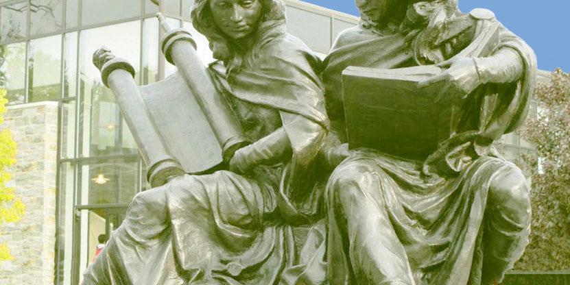 Bronzeskulptur. Nebeneinander sitzen zwei Frauen, eine mit einer Torarolle verkörpert die Synagoge, die andere mit einer Bibel verkörpert die Bibel.
