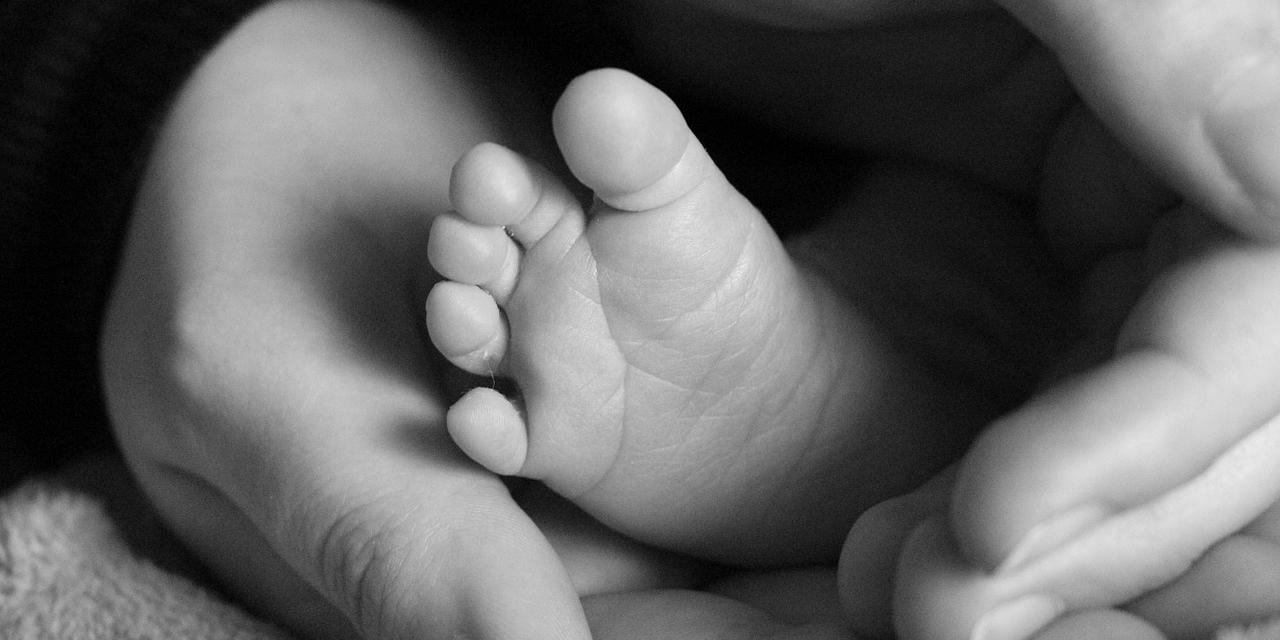 Erwachsenenhände umschließen einen Babyfuß.