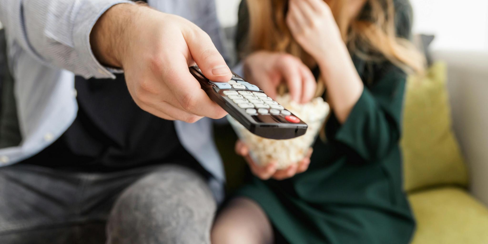 Mann und Frau auf dem Sofa mit Fernbedienung und einer Schüssel Popcorn.