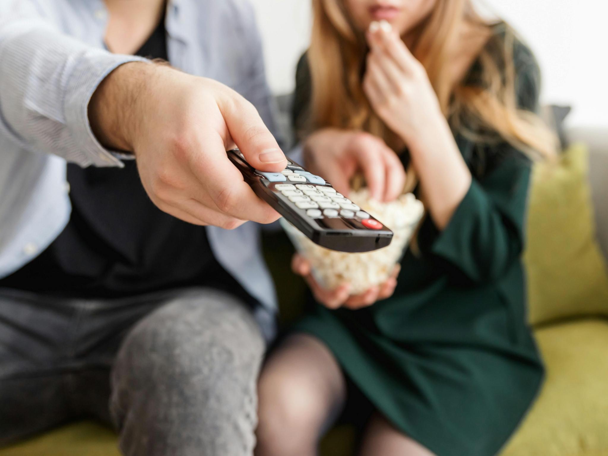Mann und Frau auf dem Sofa mit Fernbedienung und einer Schüssel Popcorn.