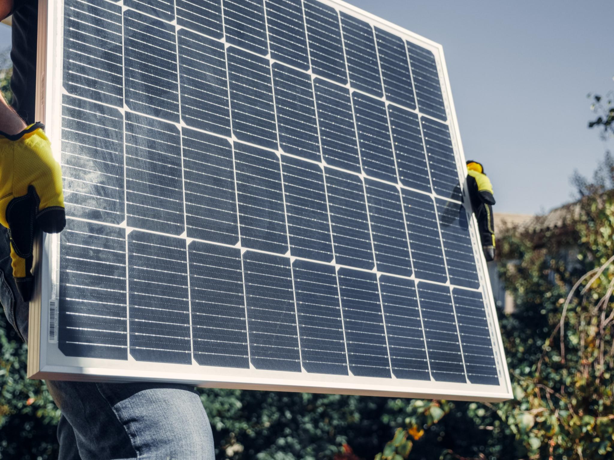 Hände in Arbeitshandschuhen halten Solarpanel